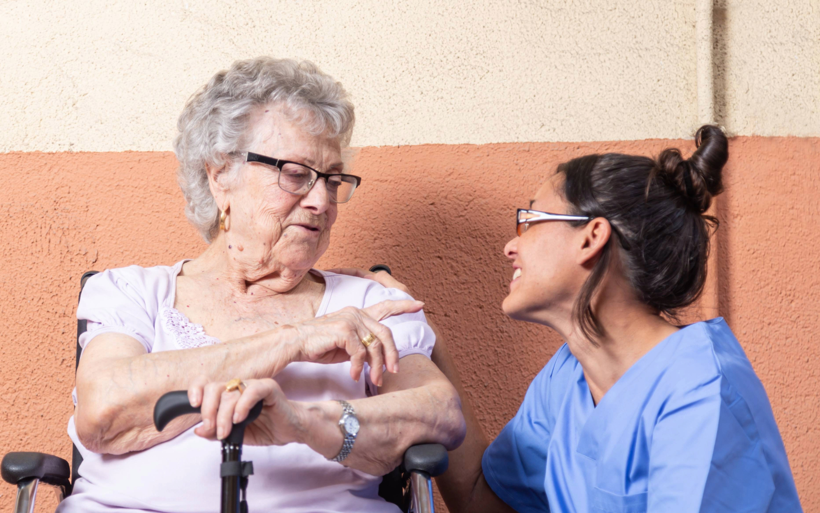 Caregiver kneeling beside an elderly person in a wheelchair, having a conversation