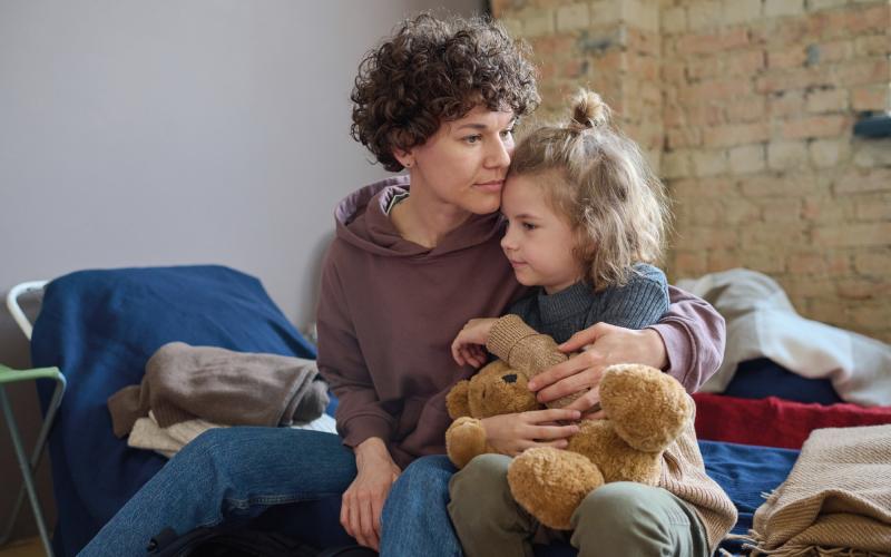 Young woman cuddles her child while both sitting on sleeping place prepared for refugees