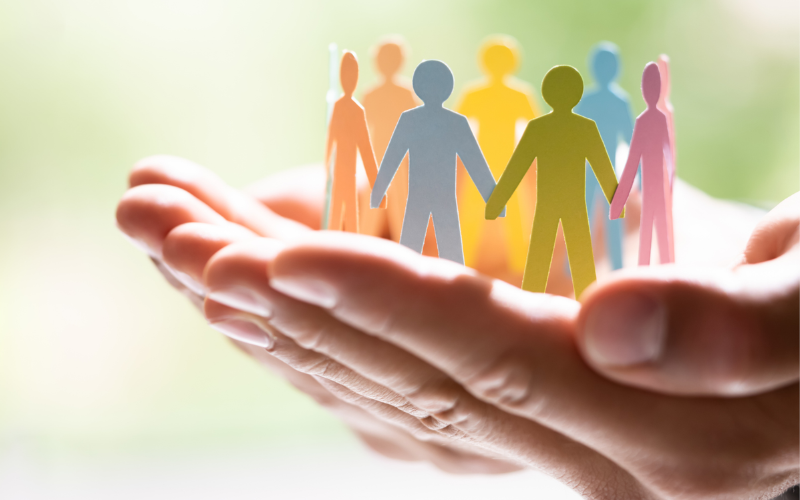 Hands gently holding a group of colorful paper cut-out figures standing in a circle.