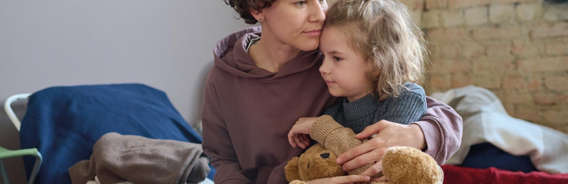 Young woman cuddles her child while both sitting on sleeping place prepared for refugees