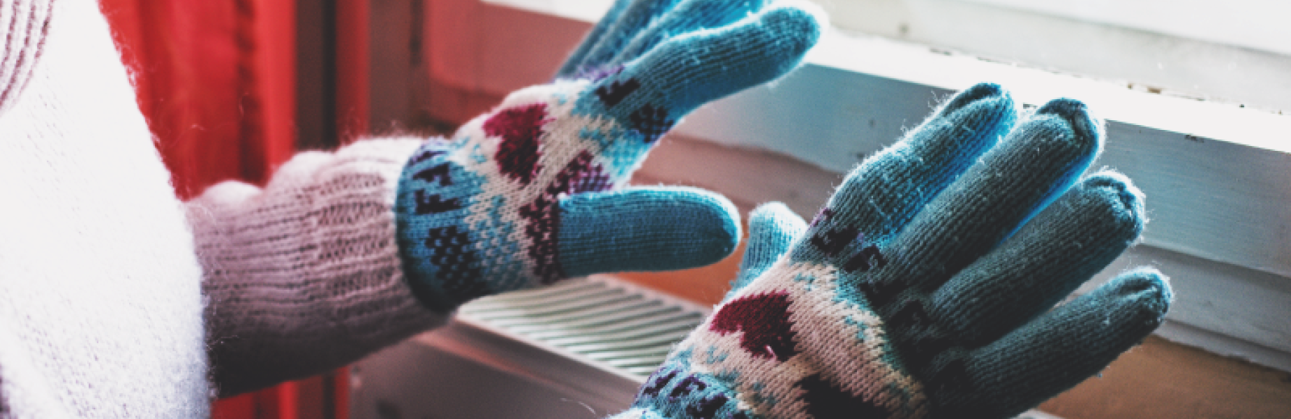 A person wearing gloves with their hands over a radiator