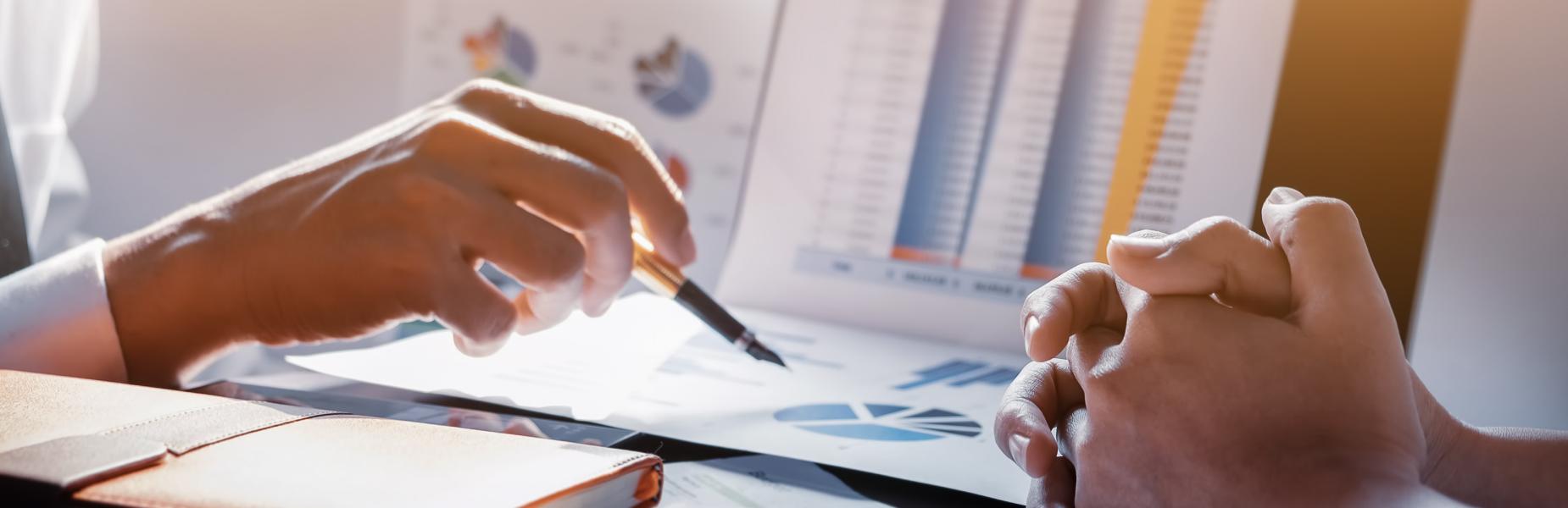 Dwylo'n trafod siartiau a graffiau ar ddesg