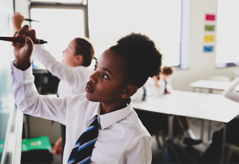 Young person in a classroom writing on a whiteboard.